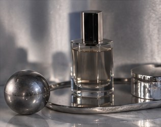 A fragrance bottle on a silver tray beside a polished metal sphere.