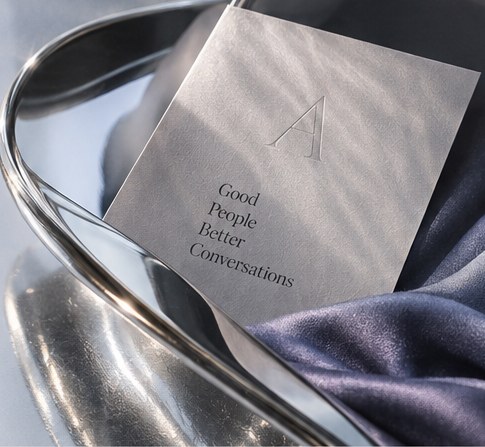 An embossed invitation card resting on a silver tray with dusty-blue satin.